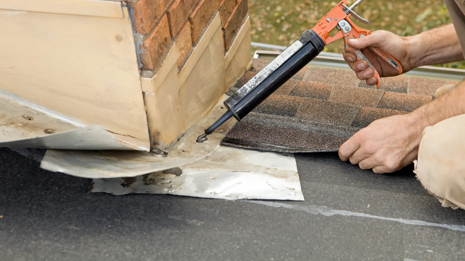 A roofer sealing chimney flashing with a caulking gun